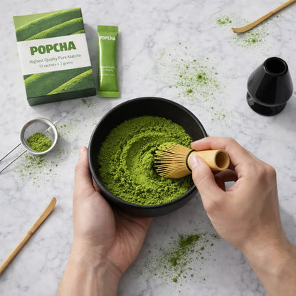 Making matcha at home with a traditional bamboo whisk set and a bowl with Popcha matcha in the background